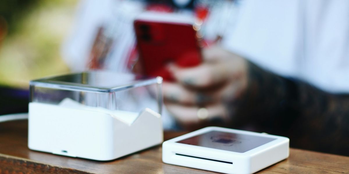 A small white payment terminal on a wooden shop counter while a customer holds up a phone to pay