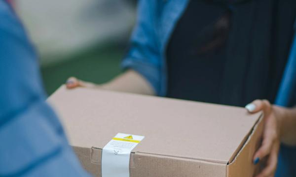Courier handing a cardboard parcel to a buyer, representing order fulfilment from both an own website and a marketplace store