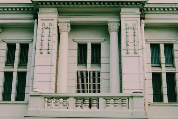 Fasad gedung kantor pemerintah bercat putih dengan deretan pilar dan jendela berterali, tempat penyedia mengurus verifikasi berkas pendaftaran LPSE