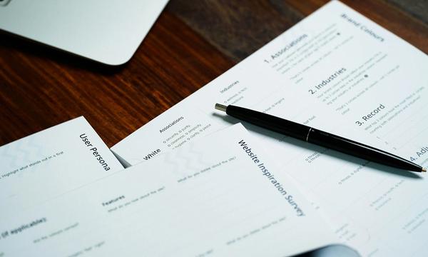 Lembar formulir pendaftaran tercetak dengan pulpen di atas meja kayu di samping laptop, gambaran pengisian data pendaftaran PSE
