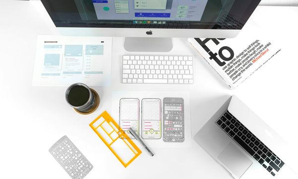 Desk with printed website wireframes, a design stencil and a computer, showing the planning stage of a web development project in Indonesia