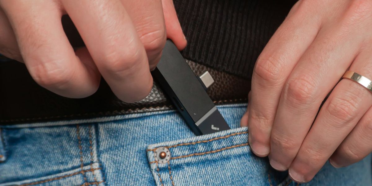 Dua tangan memasukkan hardisk SSD portabel berwarna gelap ke saku celana jins, menggambarkan salinan backup data yang dibawa keluar dari kantor