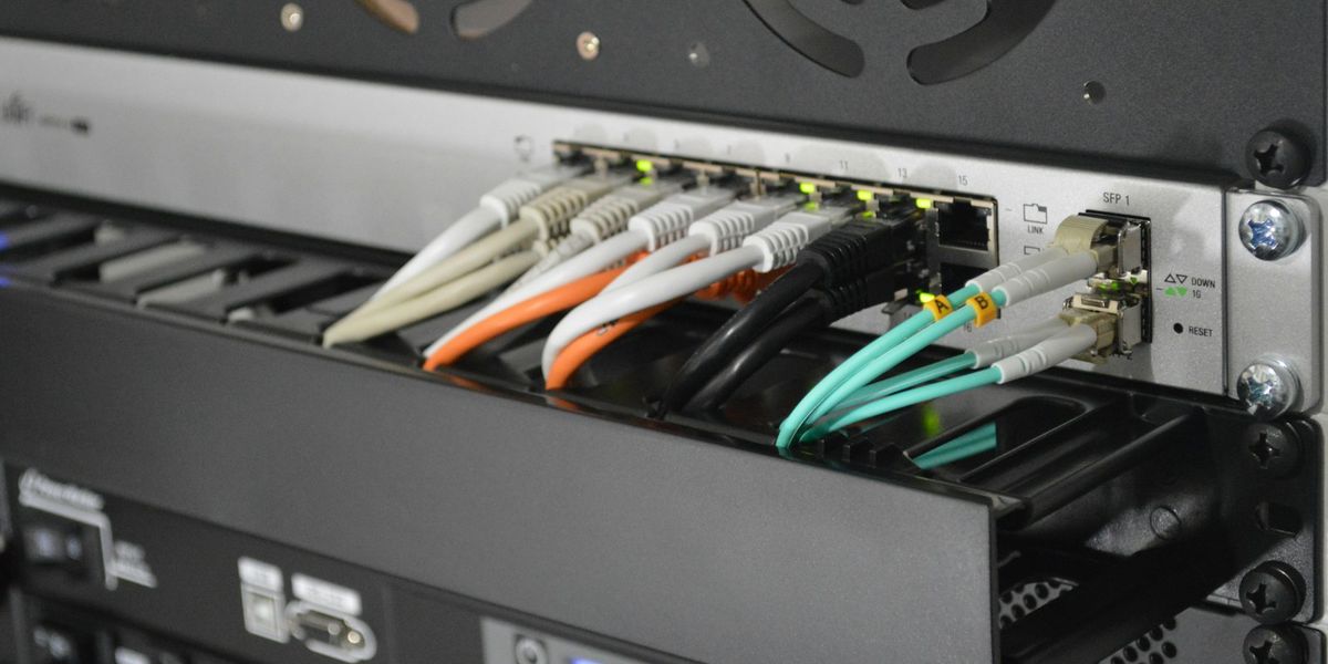 Coloured patch cables plugged into a rack-mounted network switch in an office, illustrating office network installation cost in Indonesia