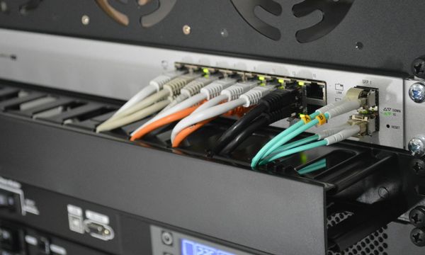 Coloured patch cables plugged into a rack-mounted network switch in an office, illustrating office network installation cost in Indonesia
