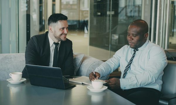Two colleagues reviewing a printed document and a laptop together at an office table, the kind of contract review that precedes affixing an electronic stamp duty in Indonesia