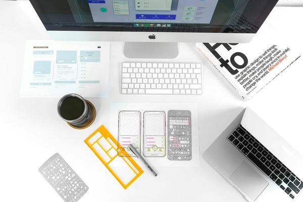 Meja kerja dengan sketsa wireframe website, stensil desain, dan komputer, gambaran tahap perencanaan saat memakai jasa pembuatan website di Sidoarjo