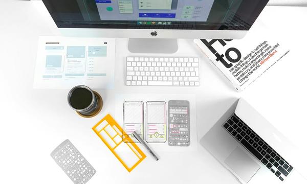 Meja kerja dengan sketsa wireframe website, stensil desain, dan komputer, gambaran tahap perencanaan saat memakai jasa pembuatan website di Sidoarjo