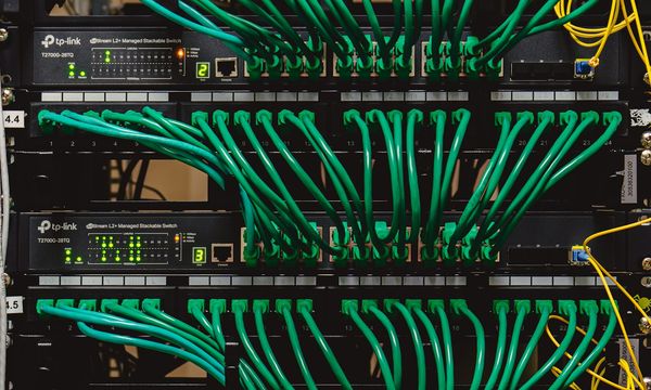 Rak jaringan kantor berisi patch panel dan switch dengan kabel patch hijau yang tertata sejajar dan masuk ke jalur kabel