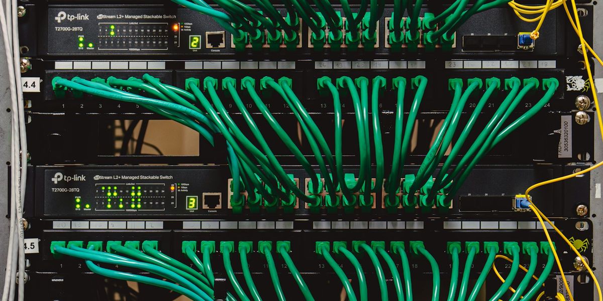 Rak jaringan kantor berisi patch panel dan switch dengan kabel patch hijau yang tertata sejajar dan masuk ke jalur kabel