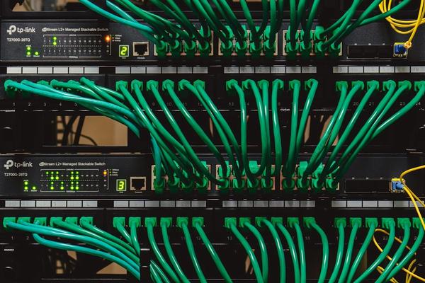 Rak jaringan kantor berisi patch panel dan switch dengan kabel patch hijau yang tertata sejajar dan masuk ke jalur kabel