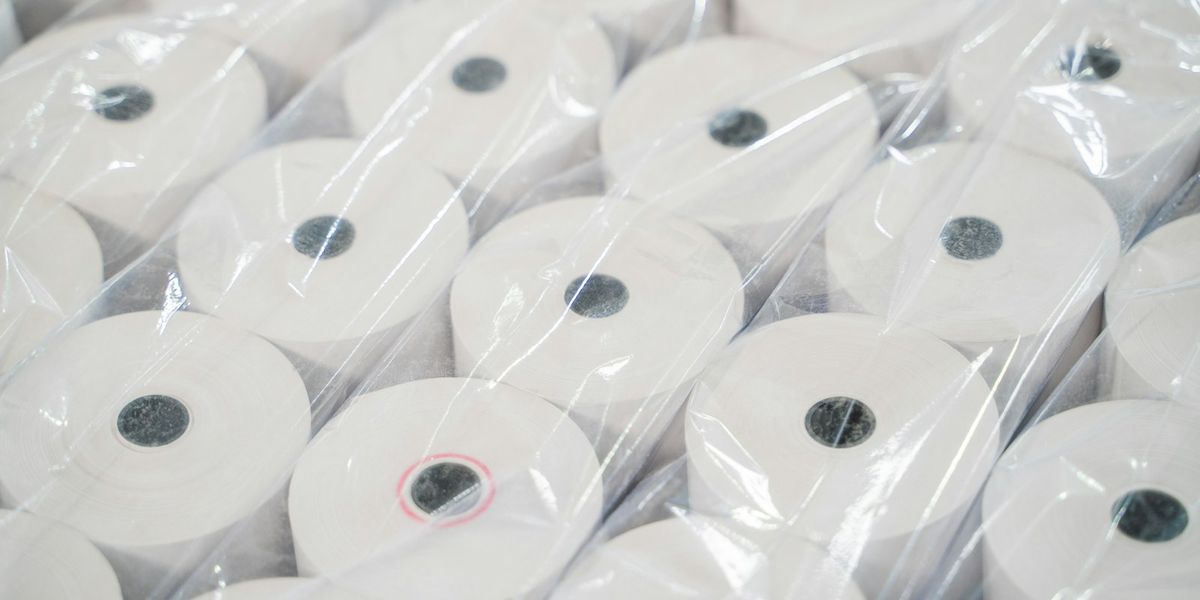 Stacked rolls of blank thermal receipt paper, the manual paperwork that automated invoicing replaces