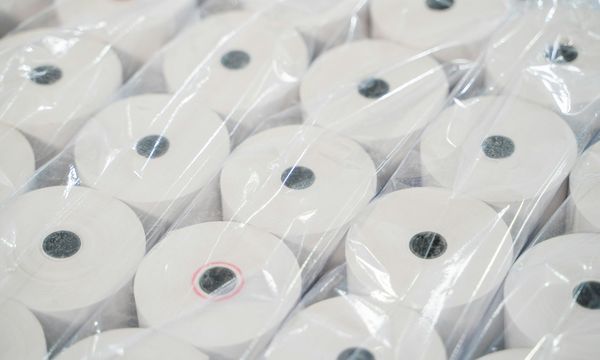 Stacked rolls of blank thermal receipt paper, the manual paperwork that automated invoicing replaces