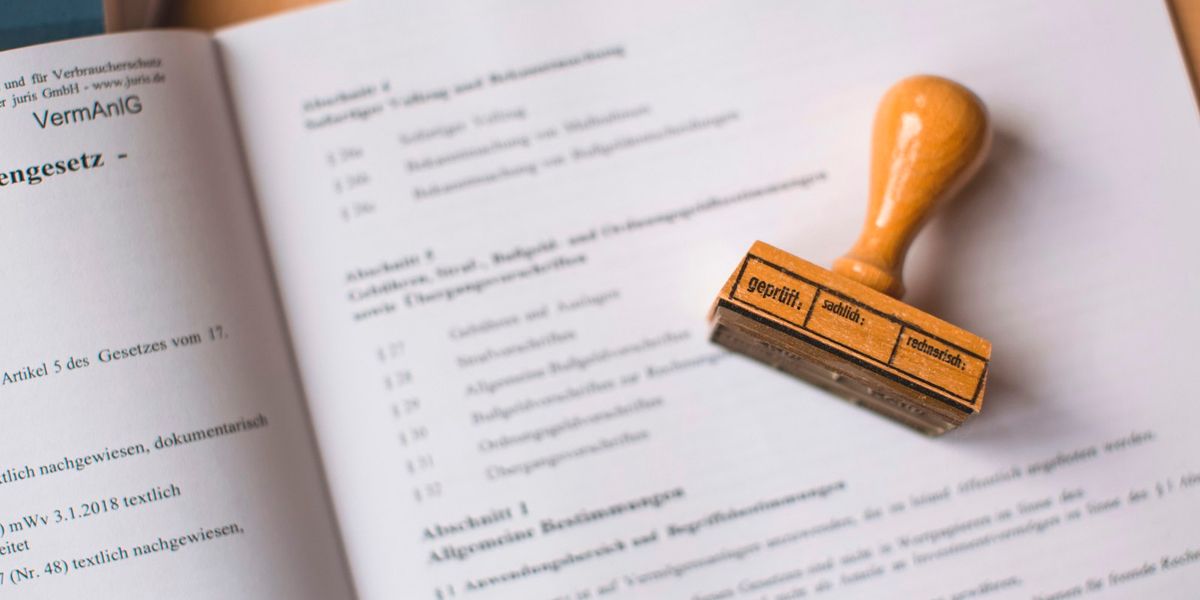 An open book of statutory regulations with a wooden approval stamp resting on the page, representing registration of a company website under electronic system rules