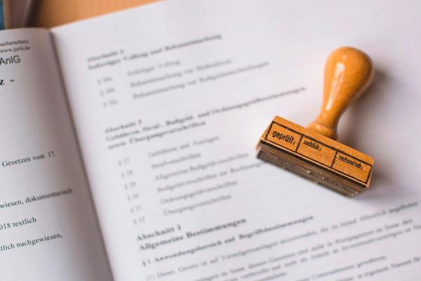 An open book of statutory regulations with a wooden approval stamp resting on the page, representing registration of a company website under electronic system rules