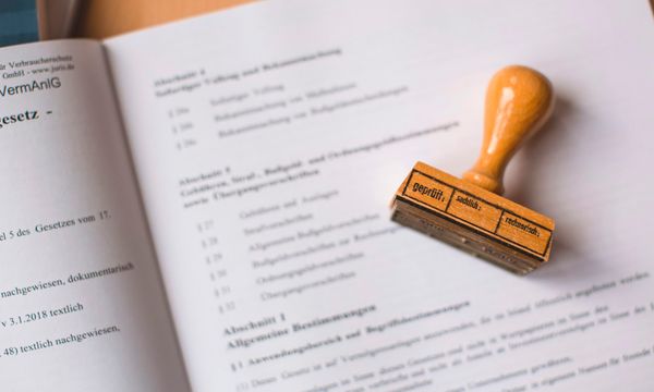An open book of statutory regulations with a wooden approval stamp resting on the page, representing registration of a company website under electronic system rules