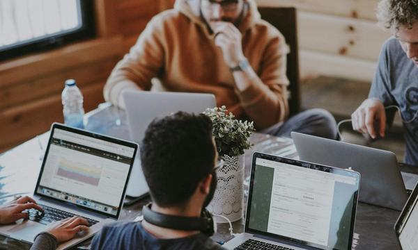 Tim pengembang web bekerja di depan beberapa laptop pada satu meja kerja, ilustrasi cara memilih jasa pembuatan website