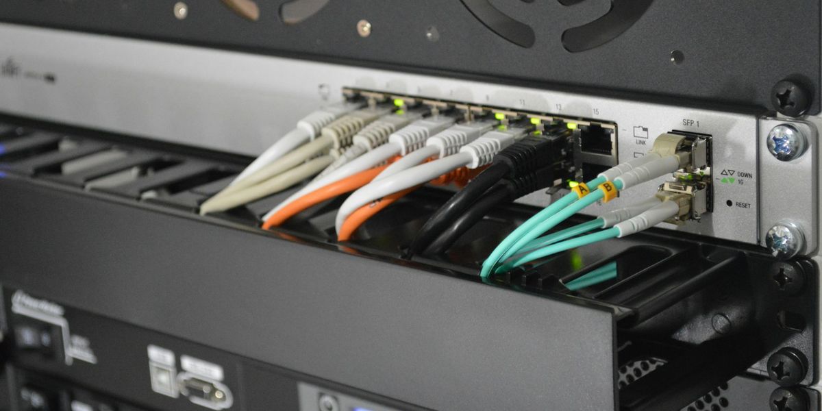 Kabel patch berwarna terpasang pada switch di dalam rack kantor, ilustrasi biaya pasang jaringan kantor