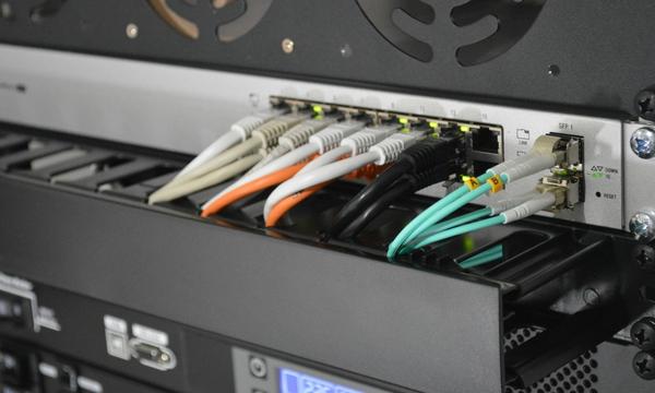 Kabel patch berwarna terpasang pada switch di dalam rack kantor, ilustrasi biaya pasang jaringan kantor