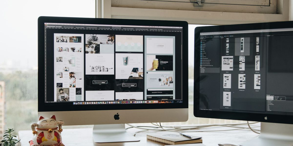 Two desktop monitors on a studio desk showing a grid of finished website page layouts, the kind of portfolio a web agency presents to a prospective client