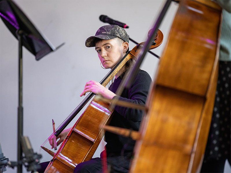 A profile shot of Kirin seated with her cello staring, her head turned intently towards the camera.