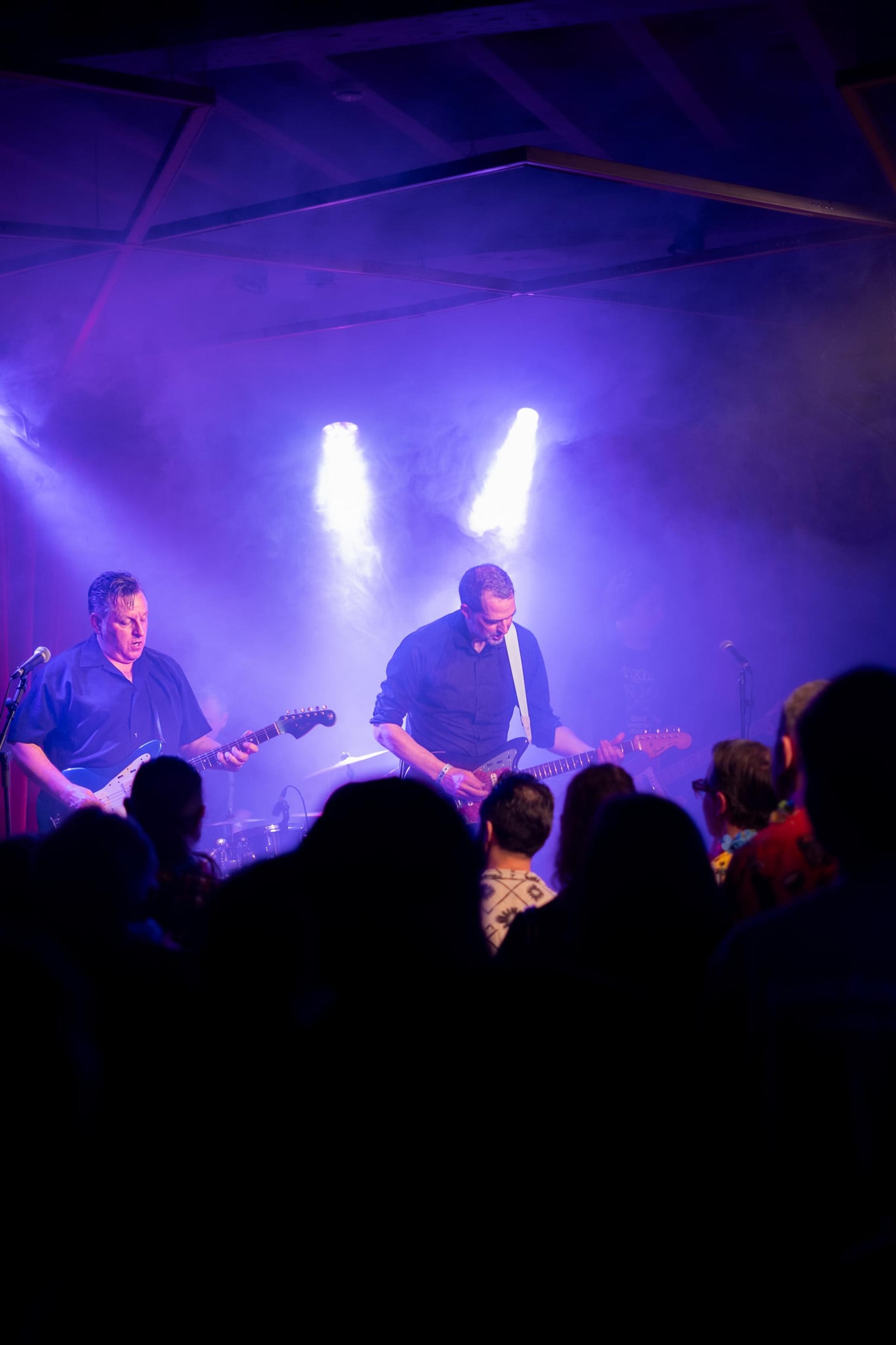 Dwóch gitarzystów w fioletowym świetle, szeroki kadr