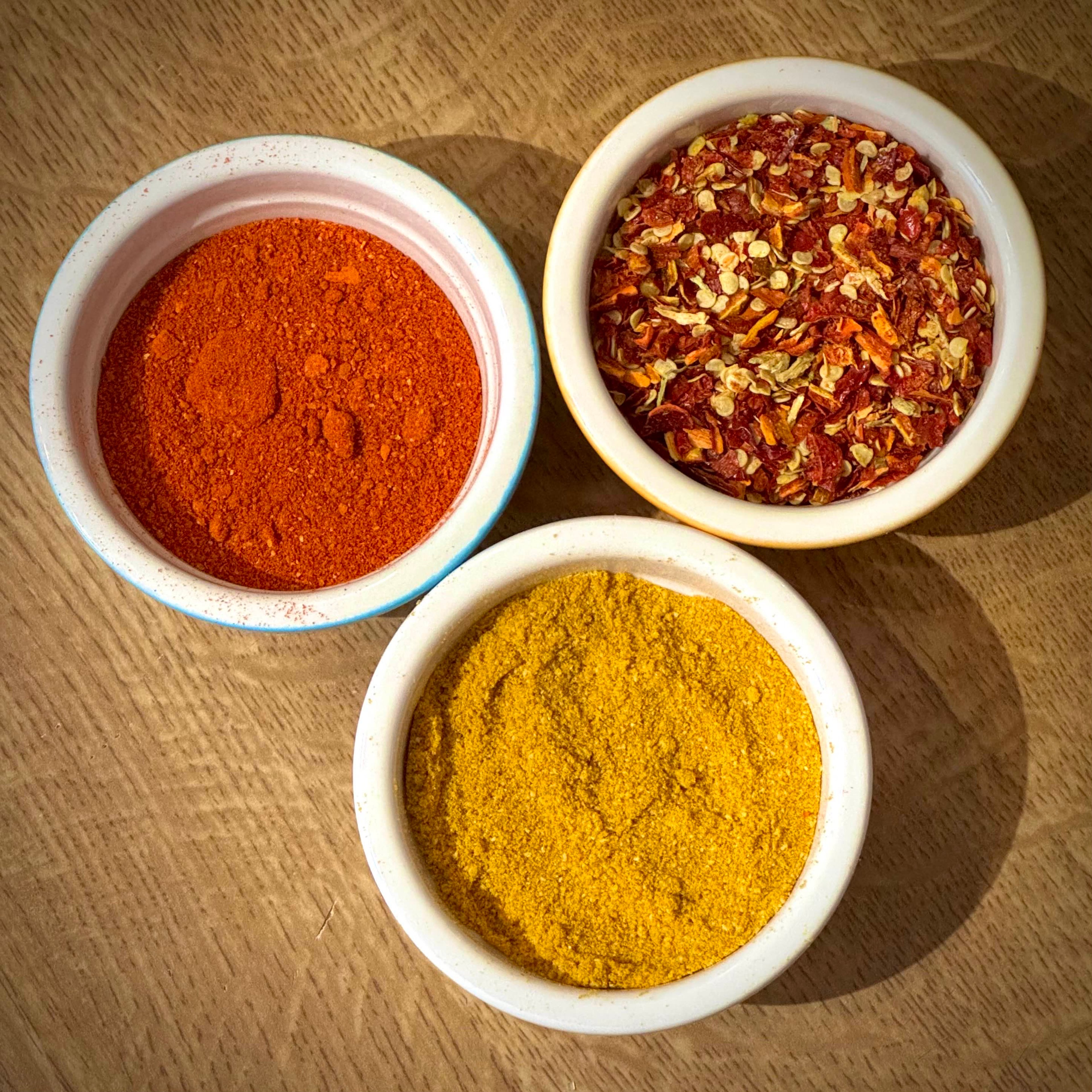 Various chili pepper powders and flakes in round containers.