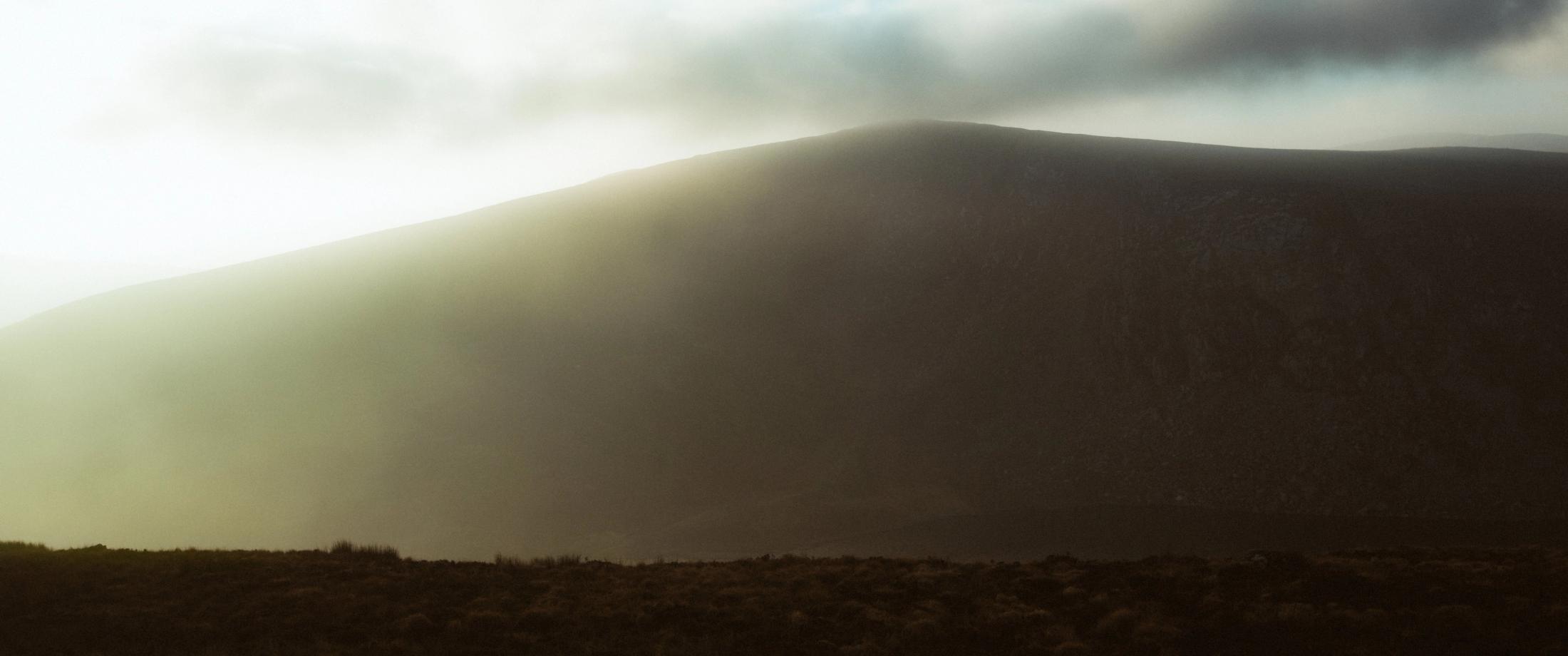 Warmes Licht fällt durch den Nebel über die Hänge der Cooley Mountains.