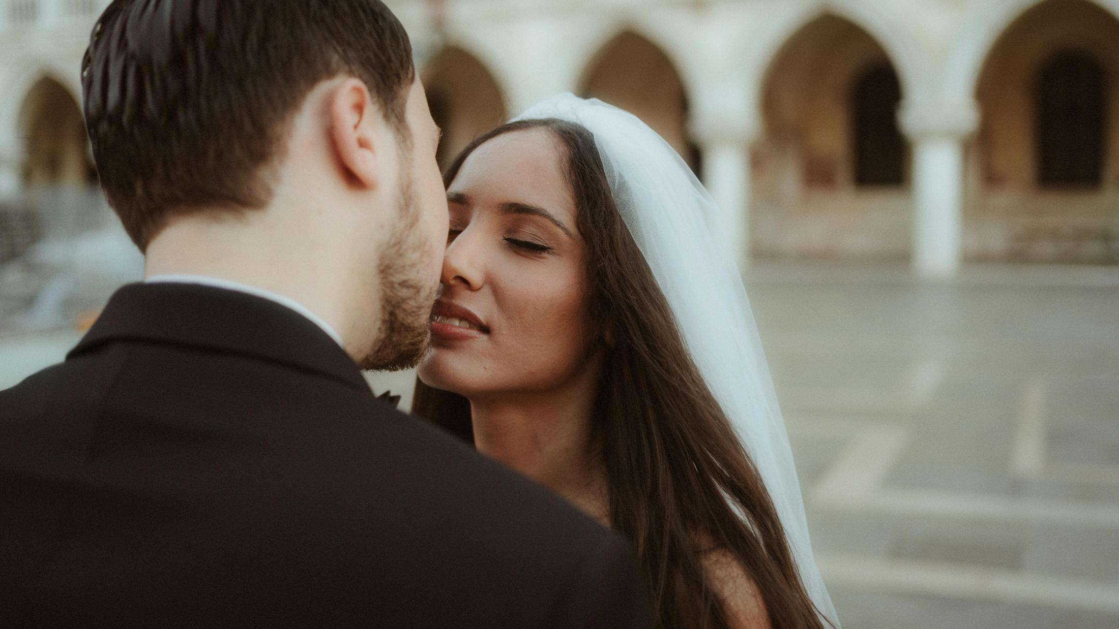 The couple leans into a kiss with Venetian arches softly behind them.