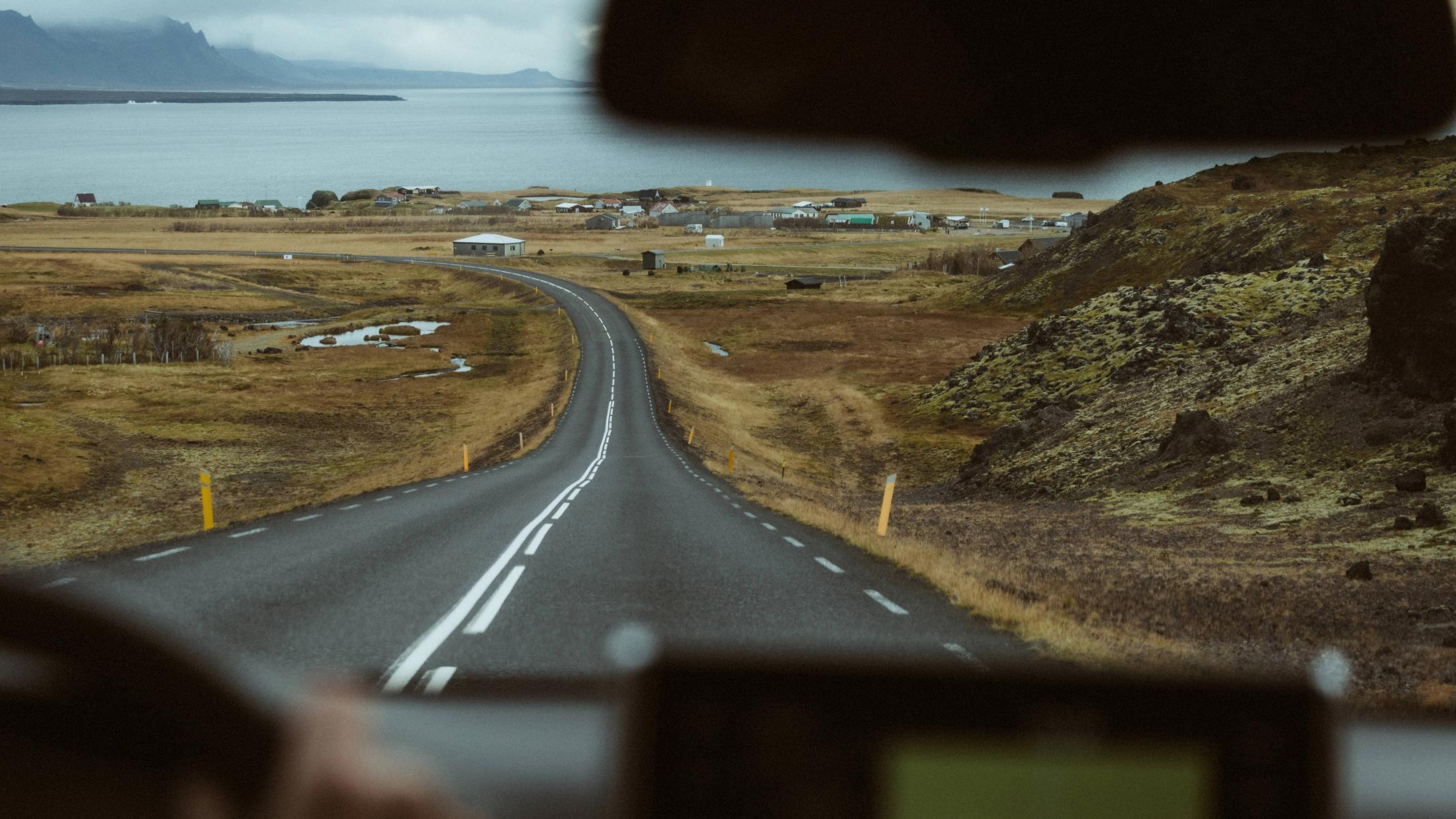 Eine leere Straße führt zwischen dunklen Hügeln durch Snæfellsnes.