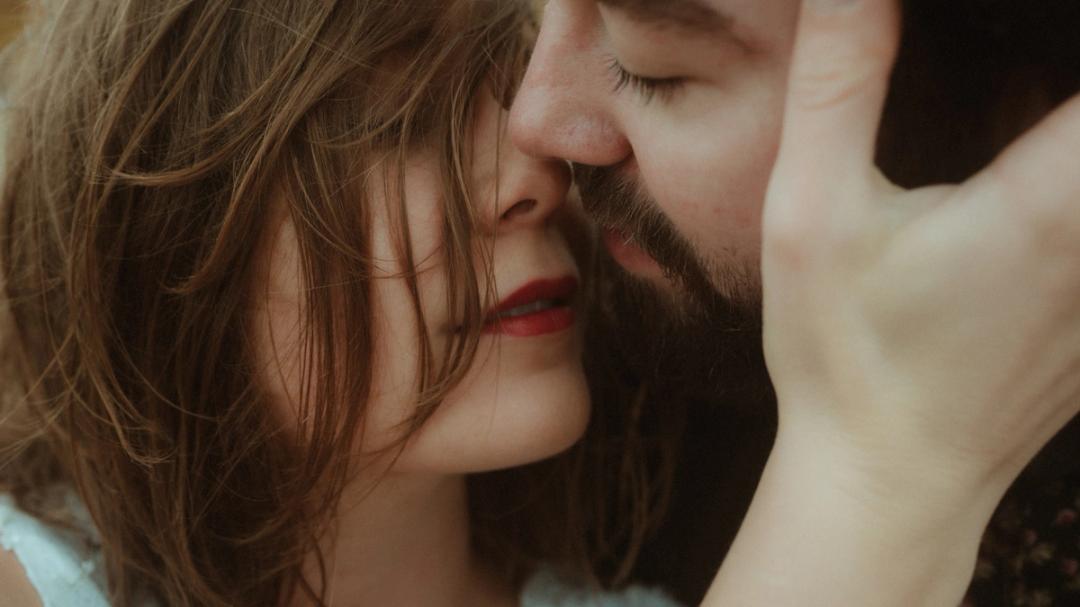 Anni frames Daniel's face with her hand during a close kiss.