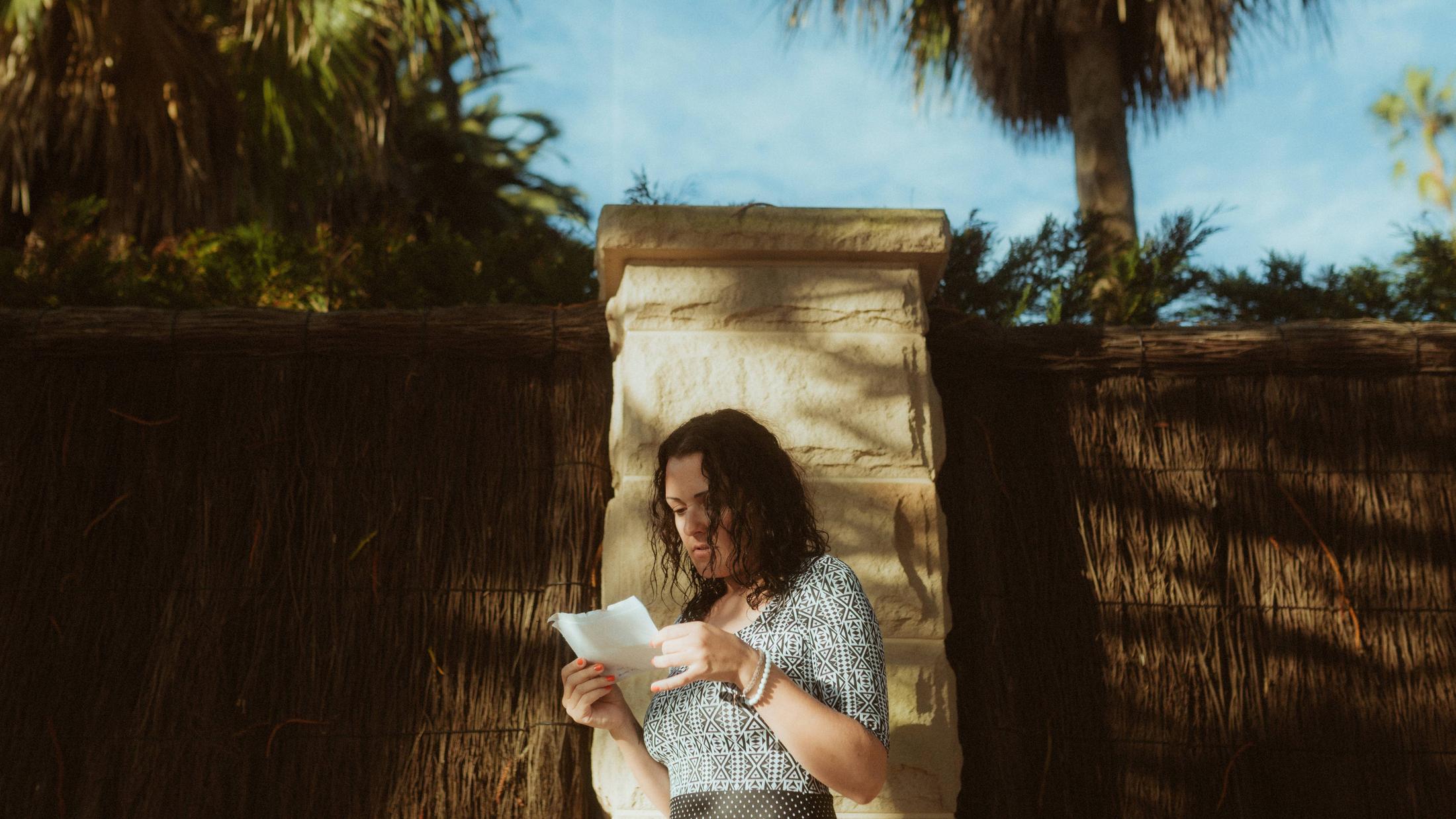 Petra reading alone beside a sunlit stone wall