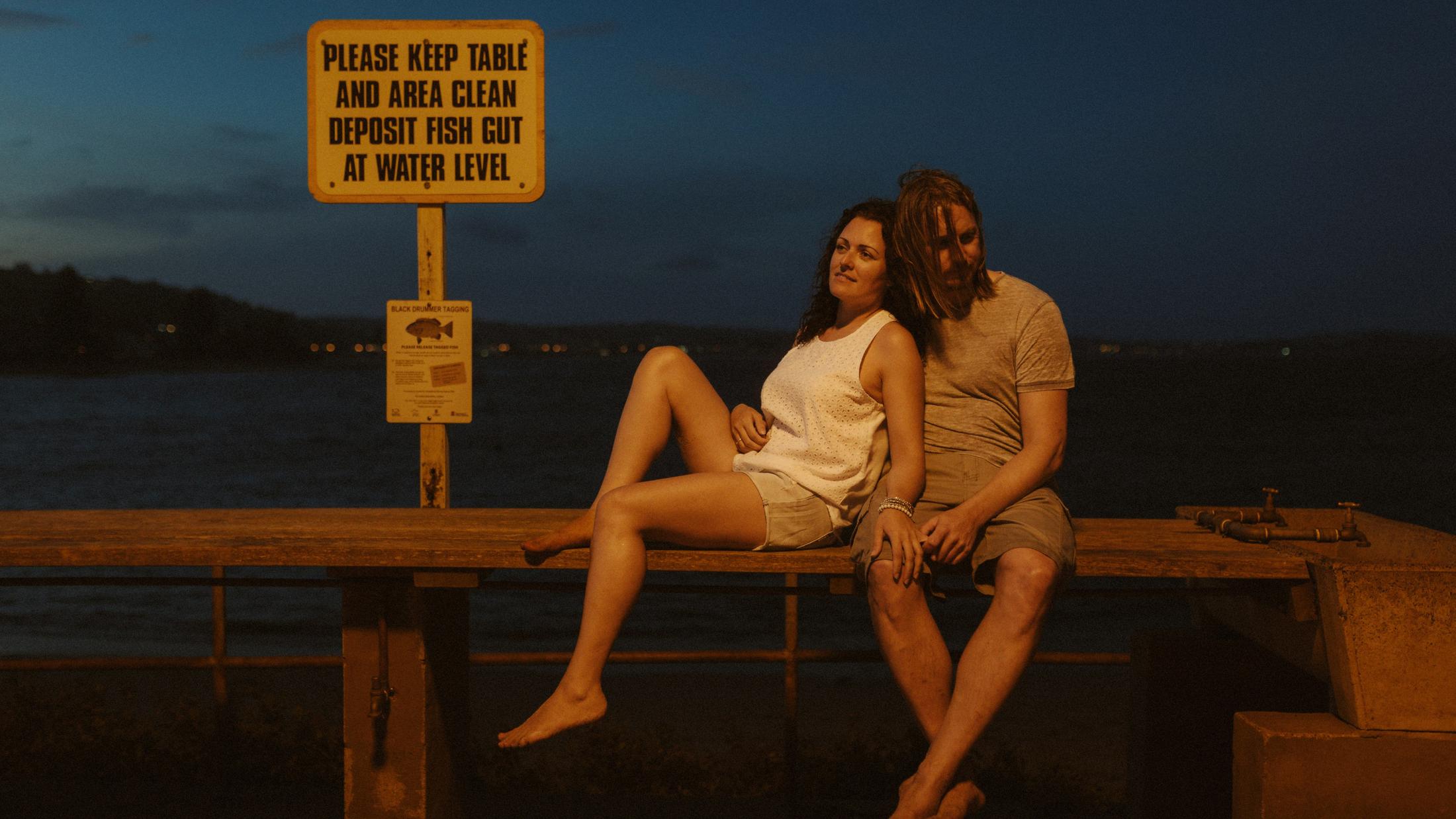 Petra and Roman sitting beneath a fish-gutting warning sign at night
