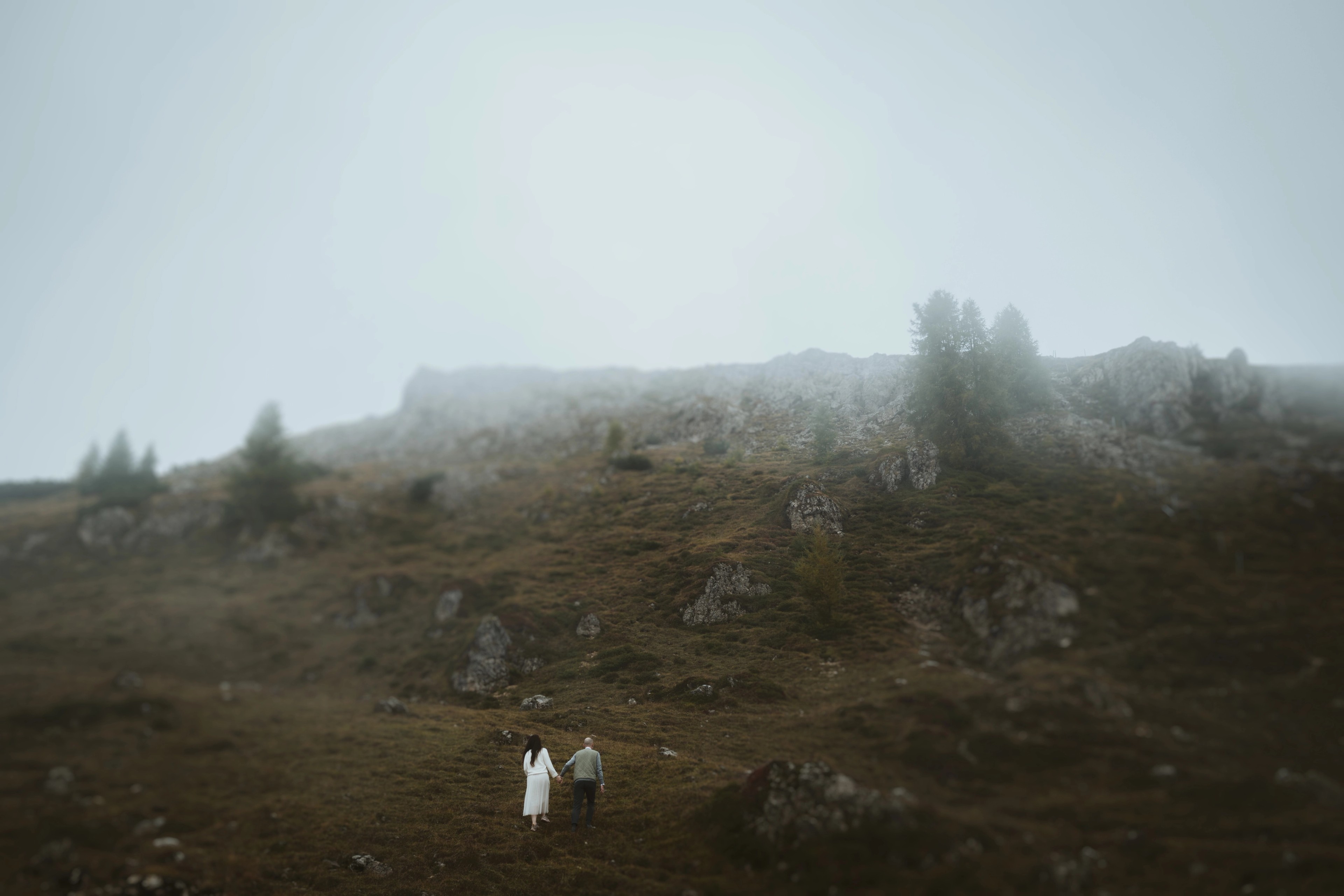 A couple walking hand in hand up a foggy mountain slope.