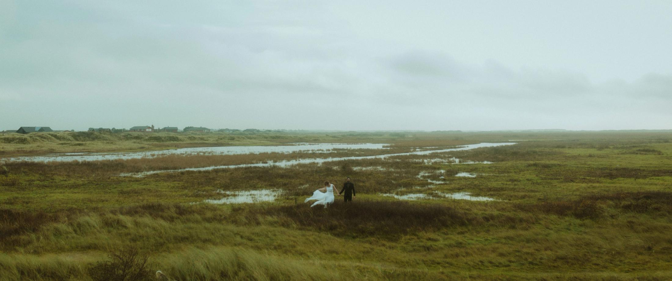 Anni and Daniel appear small in the wide marsh landscape at Lakolk Strand.
