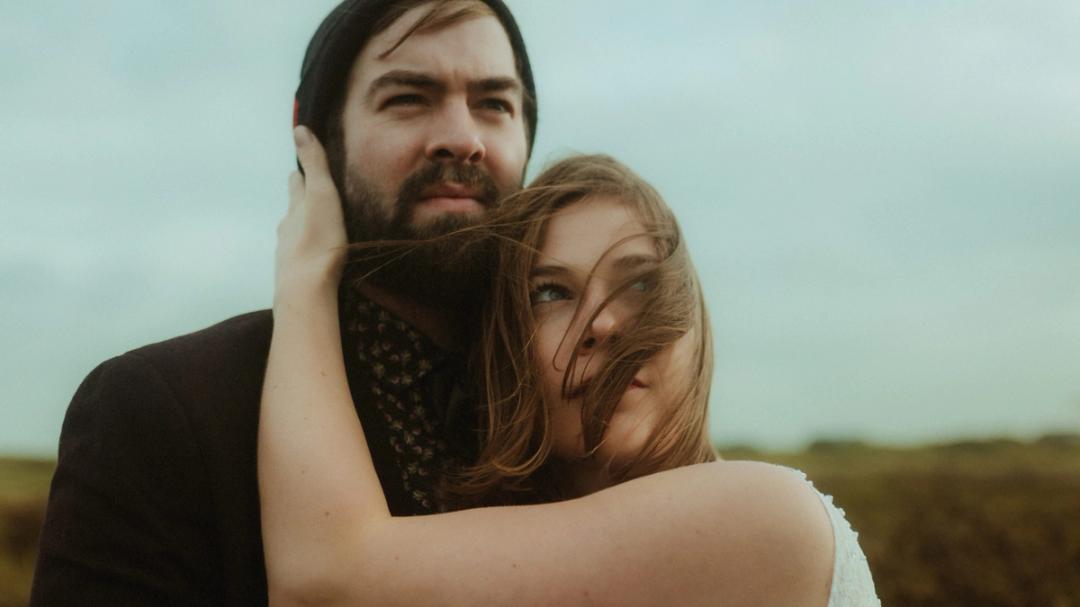 Anni holds Daniel's head as they look beyond the camera.