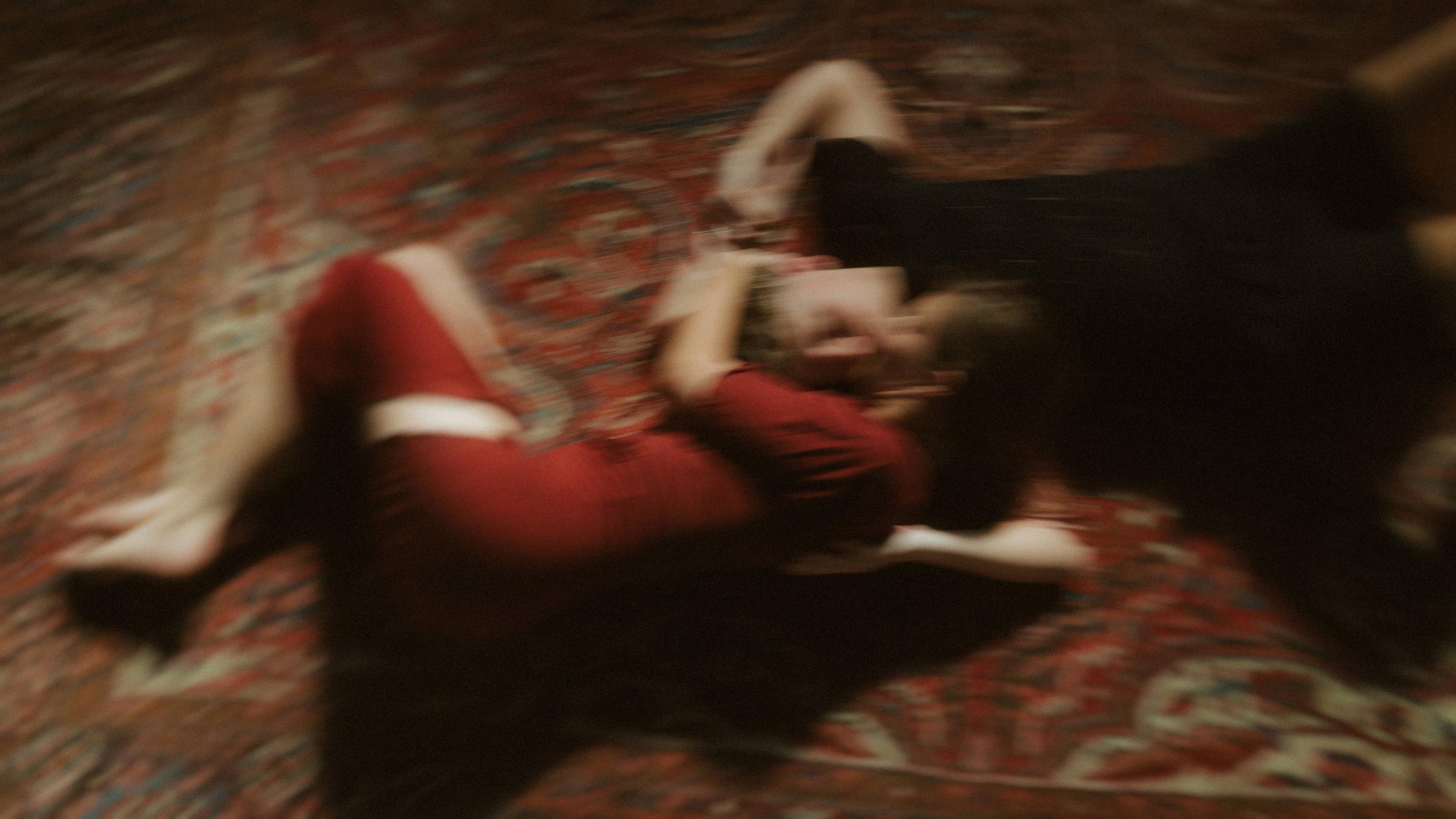 Noah and Michèle turning together on a red carpet, their bodies blurred by movement.
