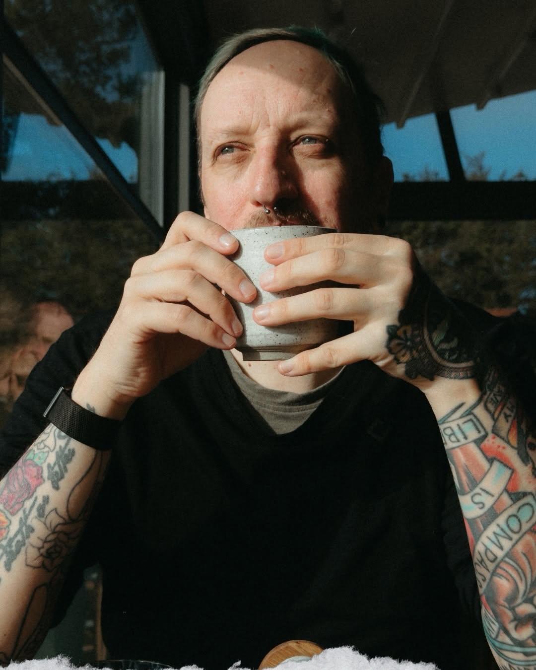 Bjørn sits by a window and drinks from a cup held in both hands.