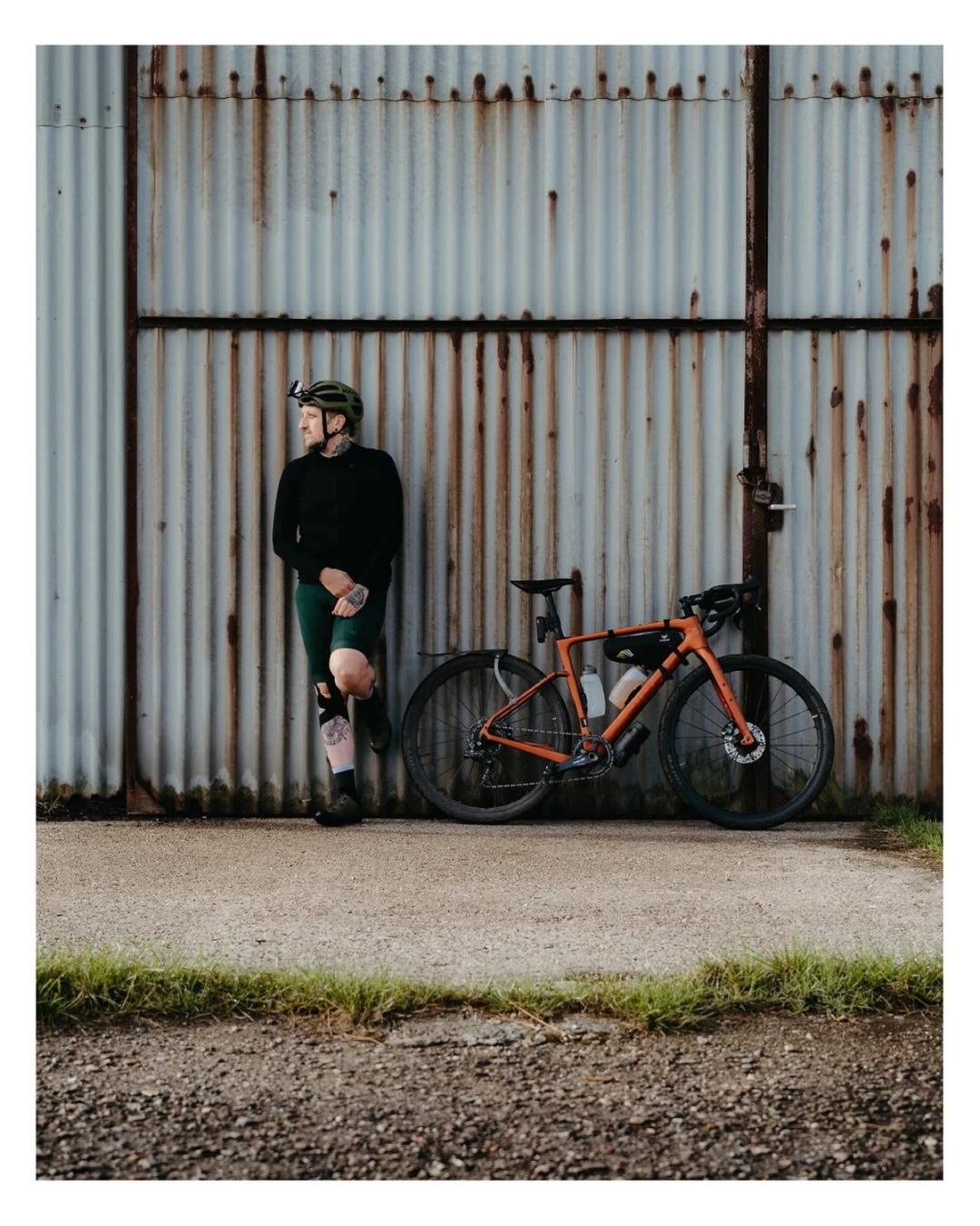 Bjørn stands beside an orange bicycle in front of a metal wall.