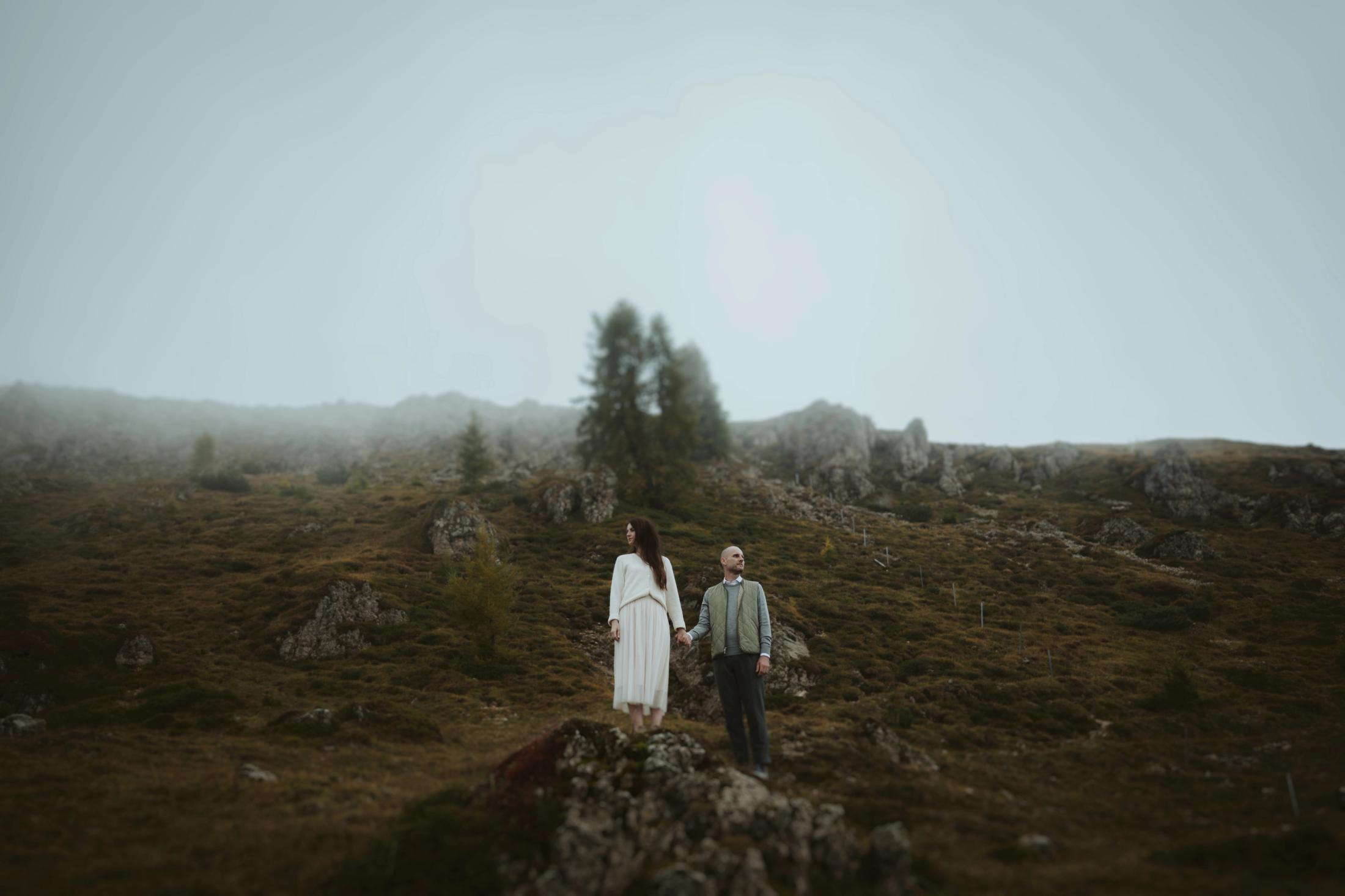Jana and Steffen standing apart on a rock surrounded by pale mountain fog.
