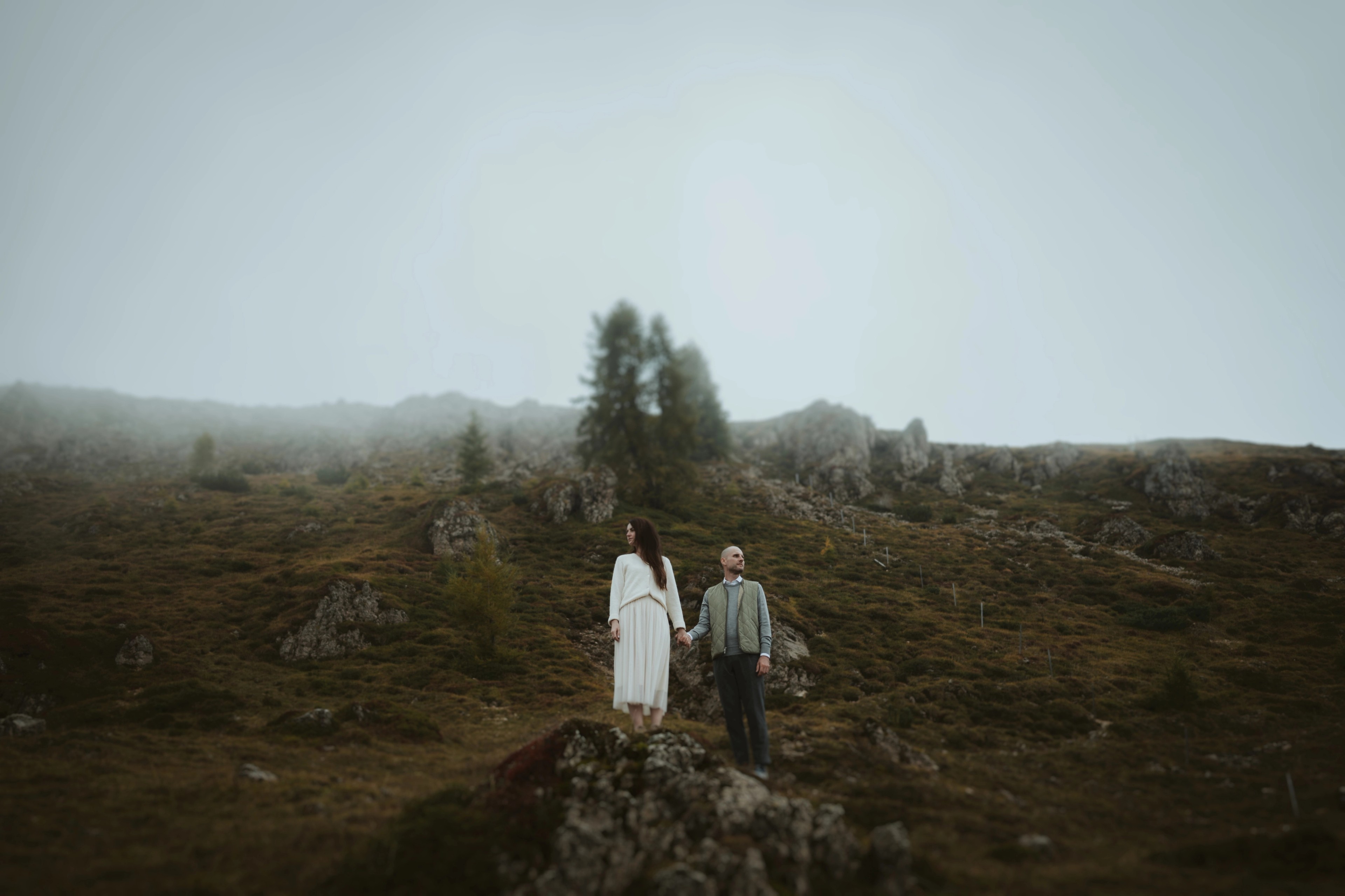 Jana and Steffen standing apart on a rock surrounded by pale mountain fog.
