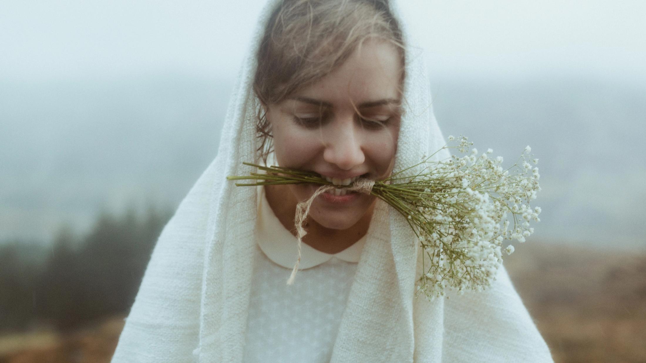 Nahporträt von Jule, die lächelnd Trockenblumen zwischen den Zähnen hält.