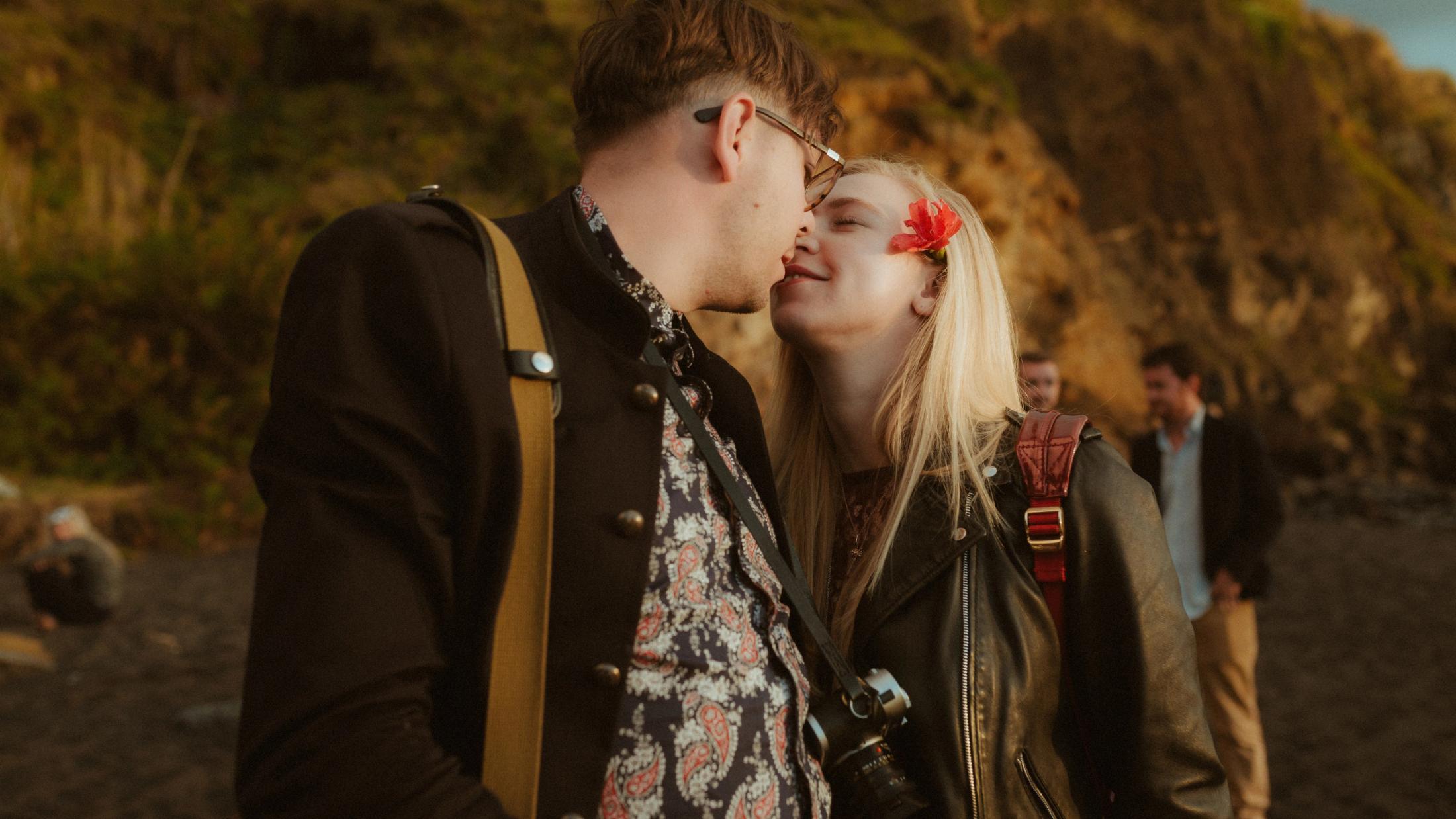 Two guests kiss while others remain gathered on the beach.