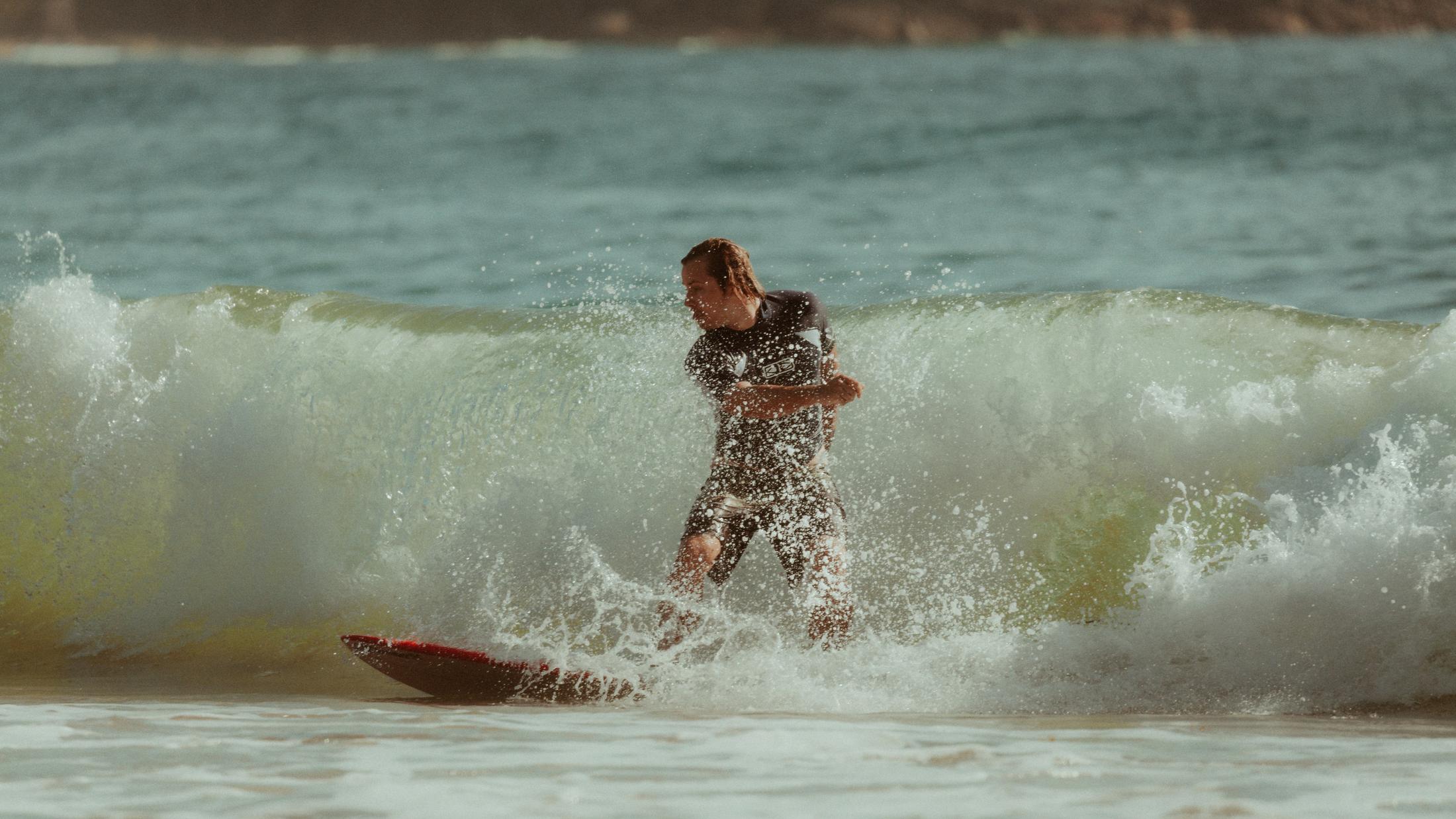 Roman losing his balance in a breaking wave beside a surfboard