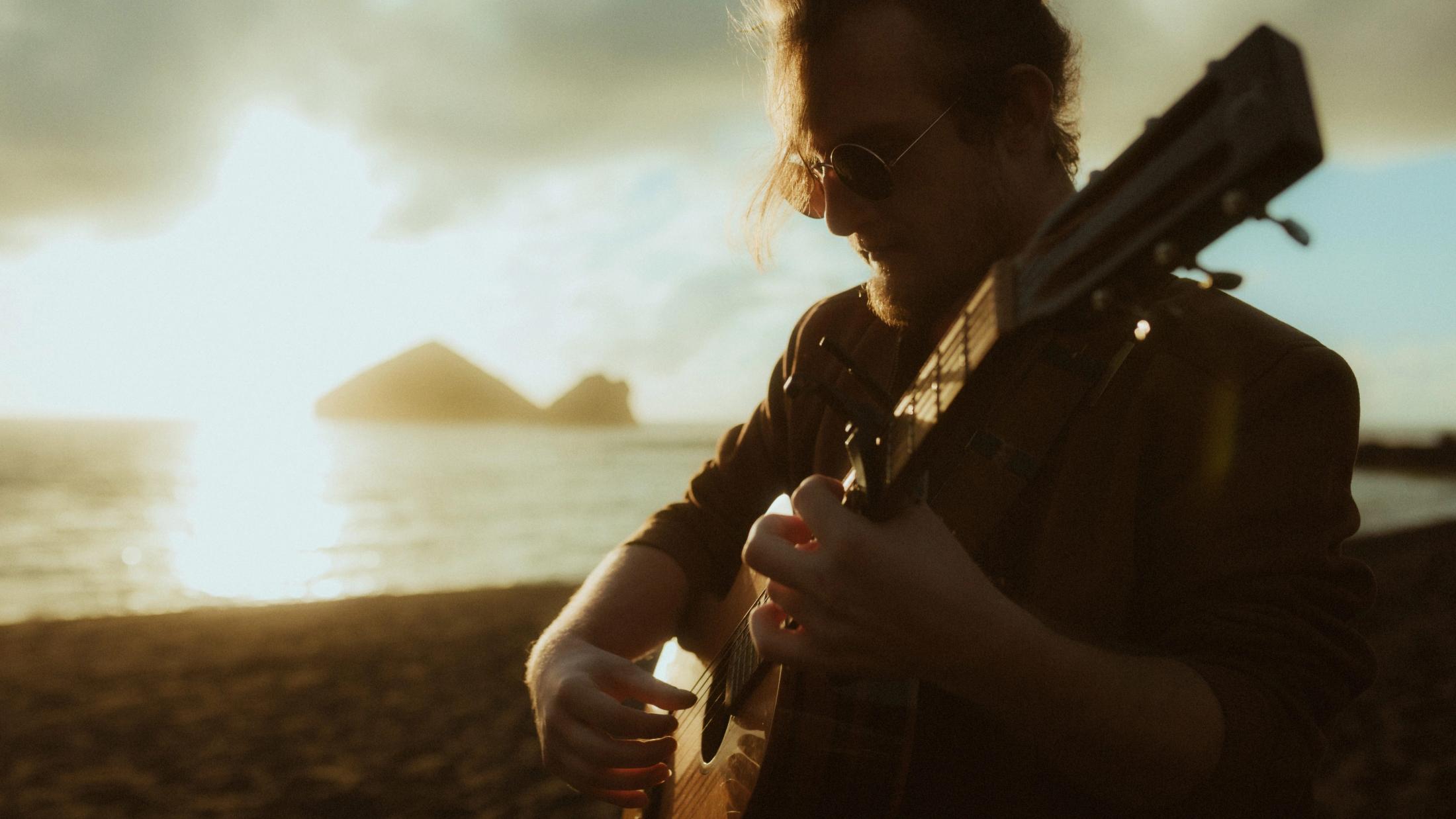 A musician plays guitar near the ceremony on the black-sand beach.