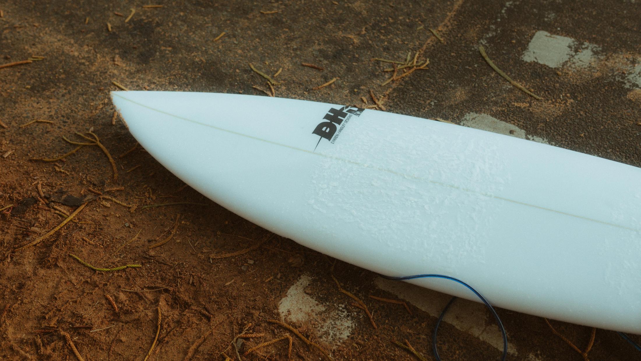 White surfboard lying on the ground beside the van