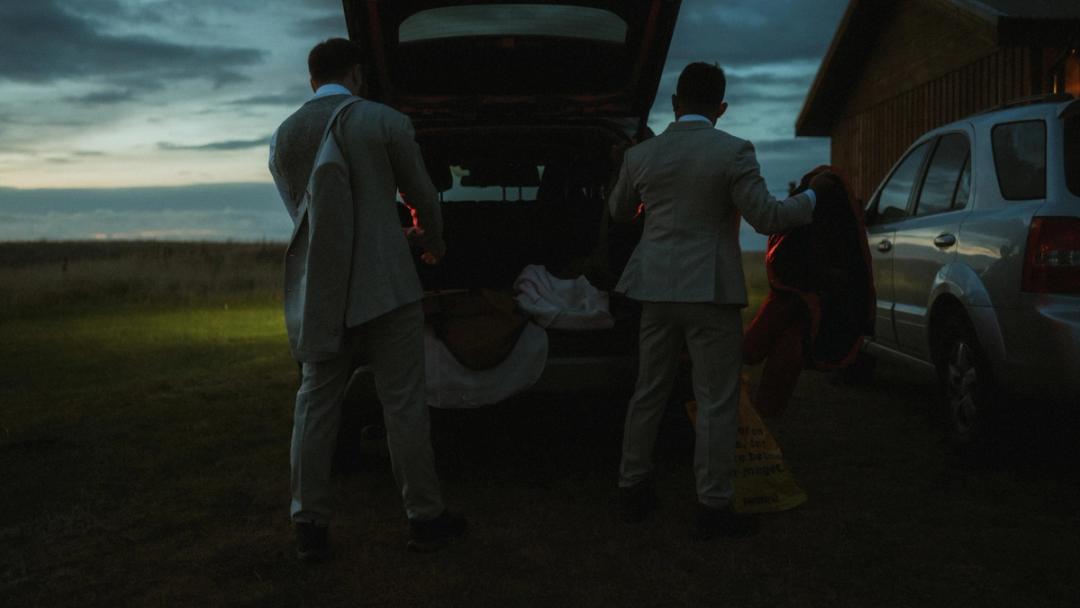 Kris and Ilya change clothes beside the open trunk of their car in Iceland.