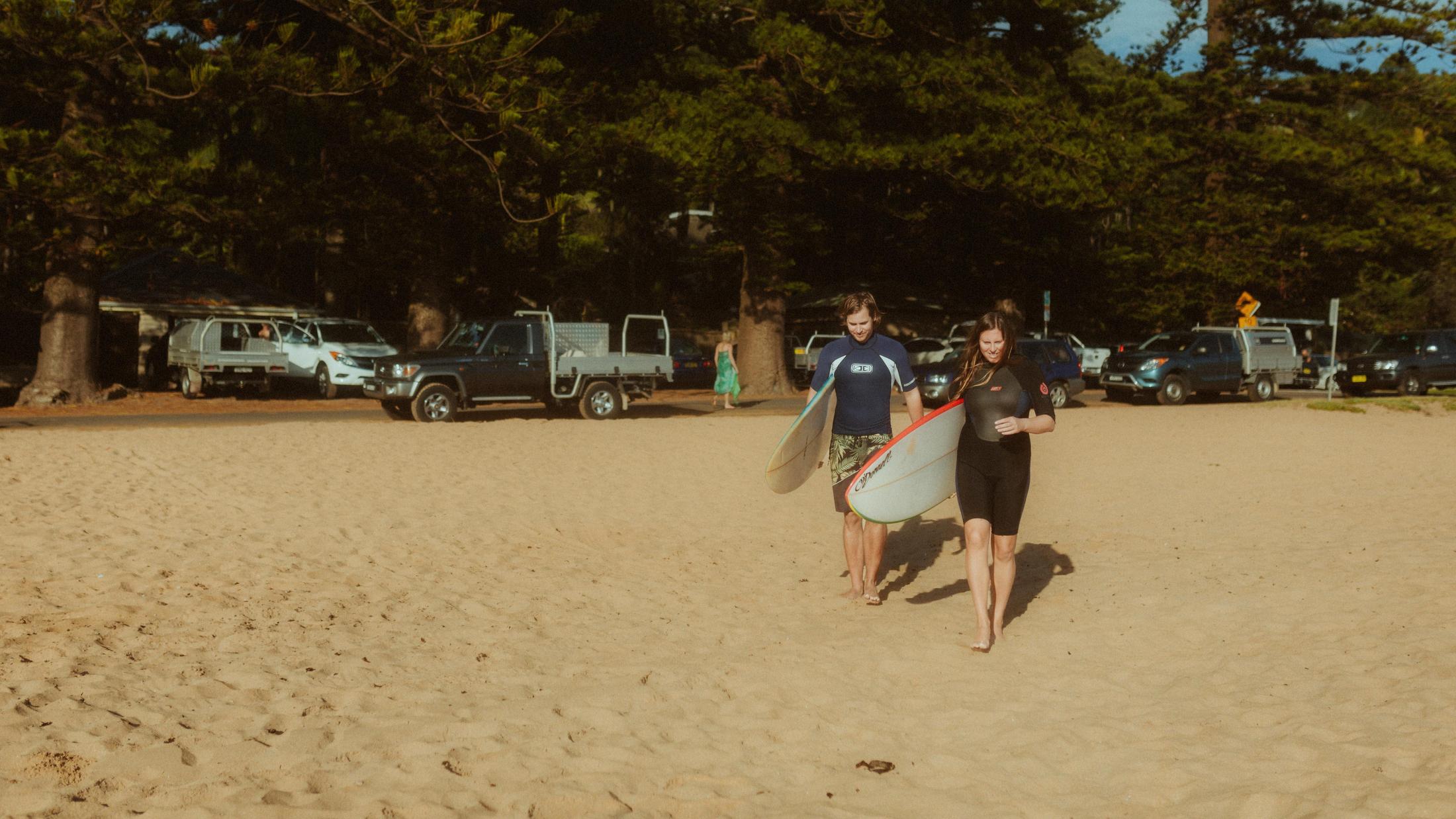 Petra and Roman walking across the sand carrying surfboards