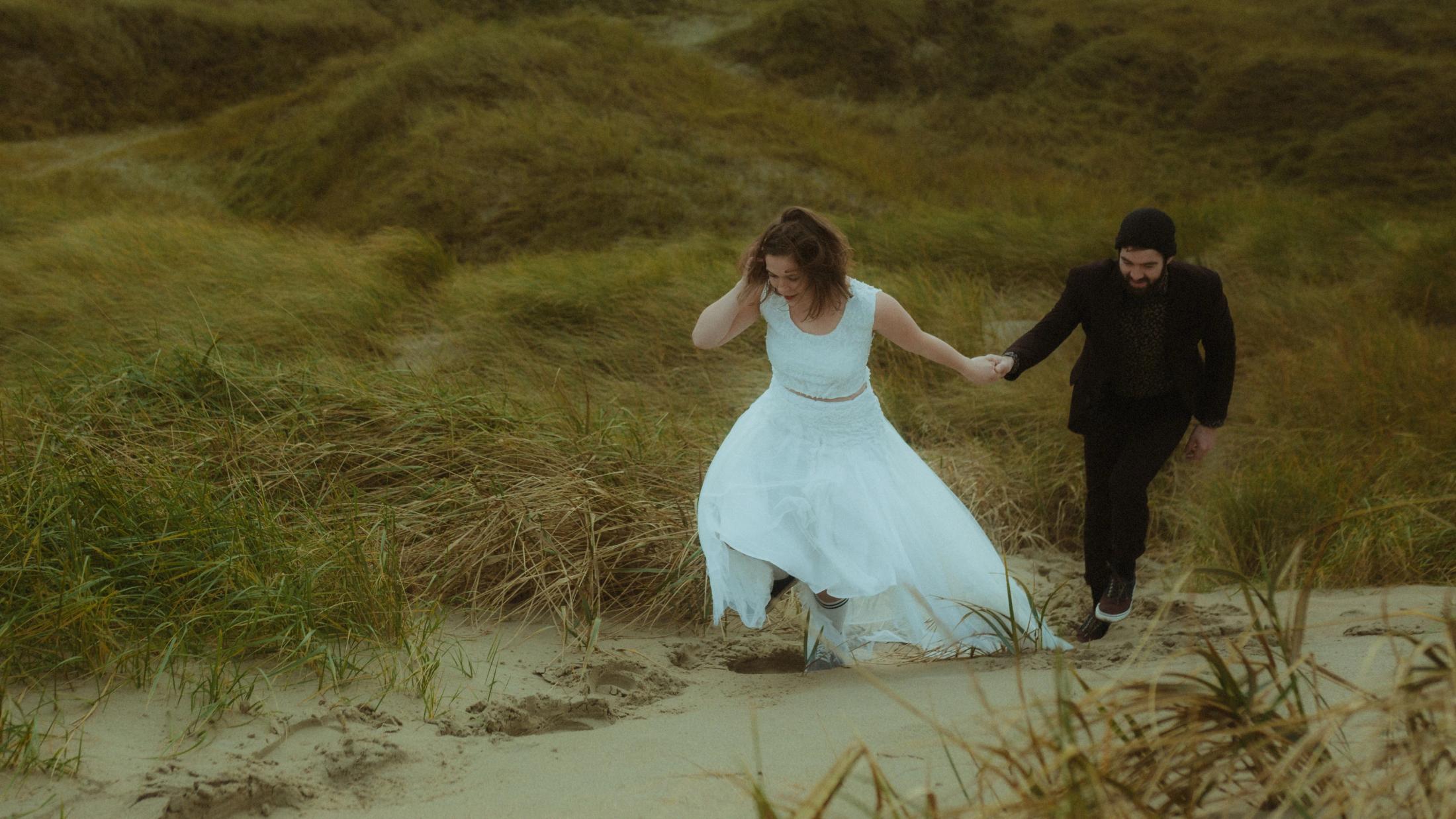 Anni leads Daniel by the hand up a sandy path between the dunes.