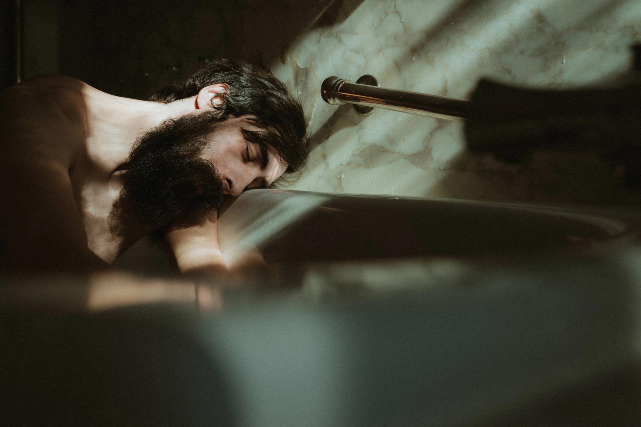 Bearded man resting in a bath crossed by window light