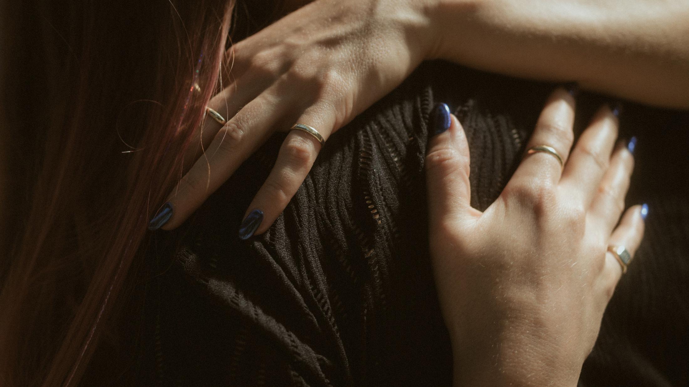 Michèle's hands resting on Noah's black shirt, with rings and blue nails visible.